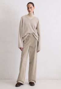 Beige oversized gebreide trui met een V-hals, gecombineerd met beige wijde corduroy broek. Bruine platform schoenen maken de outfit compleet.