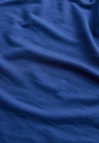 Gros plan sur un tissu bleu lisse et froissé avec une texture perforée subtile et une légère ombre.