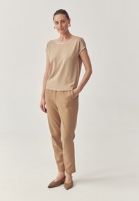 Top kaki cu mânecă scurtă, cu margini albe, purtat cu pantaloni de un maroniu deschis, cu glezne îngustate, completat de pantofi plată maro cu vârf ascuțit.