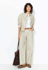 Veste beige à pois et pantalon large en tissu léger, associés à un T-shirt blanc, une ceinture marron et des chaussures à imprimé léopard marron.