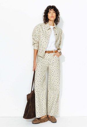 Veste beige à pois et pantalon large en tissu léger, associés à un T-shirt blanc, une ceinture marron et des chaussures à imprimé léopard marron.