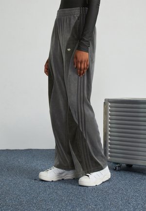 Pantalons larges en velours gris avec une taille élastique et trois bandes sur les côtés, associés à des chaussures de sport blanches.