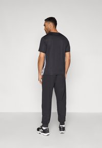 Herre træningstøj i sort, bestående af en kortærmet skjorte og joggebukser, begge med glat tekstur og detaljer med sidenstriber.