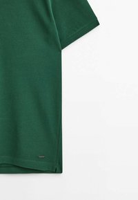 T-shirt à manches courtes vert foncé en tissu tricoté, avec une coupe droite et une petite étiquette logo en bas.