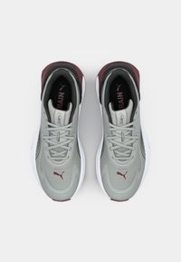 Sportssko med en grå overdel, maroon accenter og hvid sål. Har mesh tekstur, snørebånd og logo på tungen.