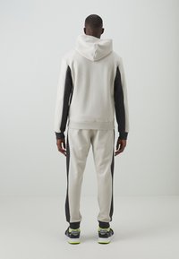 Sudadera con capucha y pantalones de chándal en un color gris claro con detalles en negro. Tejido suave, diseño ajustado y puños y cintura acanalados.