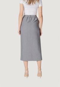 Falda gris de longitud media con una cinturilla fruncida, hecha de tela texturizada. La parte de atrás presenta un diseño de costura simple y se combina con tacones en tono nude.