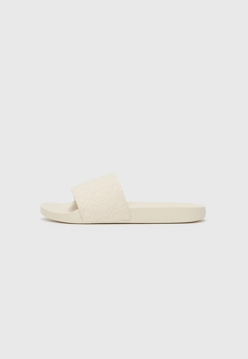 Beige Rutschsandale mit einem strukturierten Obermaterial, das ein sich wiederholendes Muster aufweist. Weiche Sohle mit glatter Oberfläche, leicht abgerundete Zehenform.