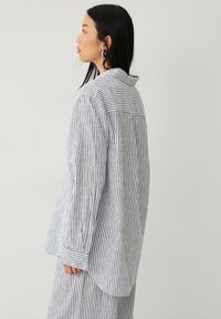Camisa de botones a rayas en mezcla de algodón, con rayas verticales azules y blancas, cuello, mangas largas y dobladillo curvado.