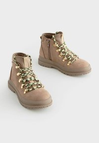 Stivaletti alla caviglia in suede beige con lacci a motivo verde e nero e dettagli in metallo dorato, dotati di cerniera laterale e suola in gomma testurizzata.