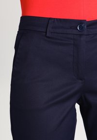 Navybyxor med en slät textur, med knappstängning fram och sidofickor. Tillverkade av ett lätt tyg, skräddarsydd passform.