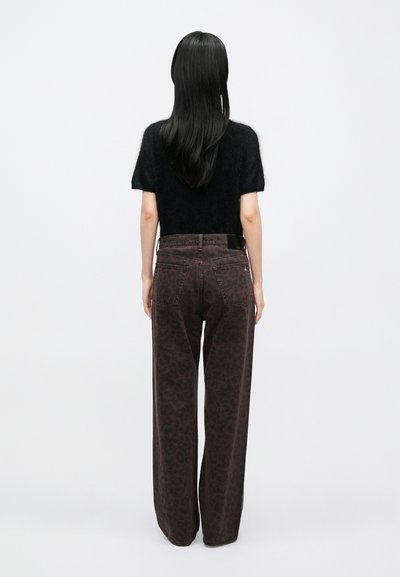 Čierny huňatý top s krátkym rukávom v kombinácii s vysokým pásom, širokými nohavicami s tmavým leopardím vzorom a opaskom.