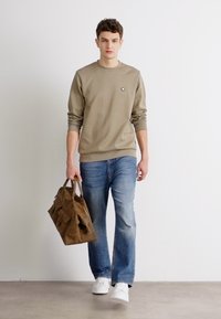Beige sweatshirt with ribbed cuffs, blue jeans, and white sneakers. Brown bag with multiple pockets. Simple design, casual look.