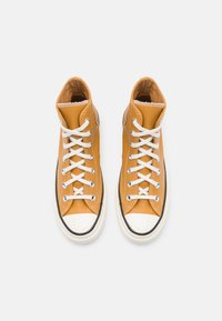 Baskets montantes en cuir jaune moutarde avec lacets blancs, bout rond blanc, et coutures contrastantes sur les panneaux latéraux texturés.