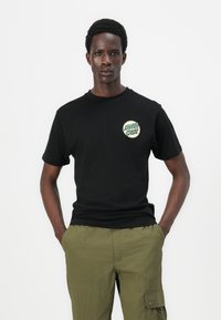 Black cotton t-shirt with short sleeves, featuring a green and white circular graphic that reads "SANTA CRUZ" on the left chest.