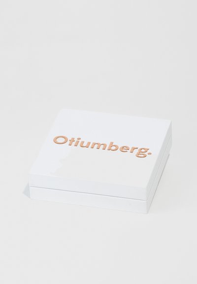 Bijela kvadratna kutija glatke teksture, s uzdignutim, svijetlosmeđim uvučenim logotipom "Otiumberg" na gornjoj površini.