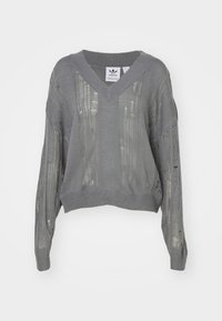 Grå stickad tröja med V-ringning, vida ärmar och öppet stickad struktur. Har dekorativa mönster och subtila ribbade detaljer i fållen.