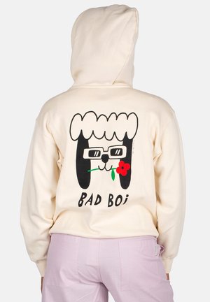 Cremfarbener Hoodie mit einem cartoonhaften Charakter mit Brille, einer Blume und dem Text "BAD BOI" auf der Rückseite. Weicher Stoff, lockere Passform.