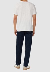 Witte T-shirt met korte mouwen en een losse pasvorm, gecombineerd met donkerblauwe broek en lichte schoenen met beige accenten. Eenvoudig, casual ontwerp.