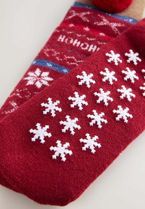 Sarkans ziemas zeķes ar teksturētu adījumu, baltām sniegpārsliņām un pūkainu pom-pomu uz atloka. Iekļauta kontrastējoša zilā lentes detaļa.