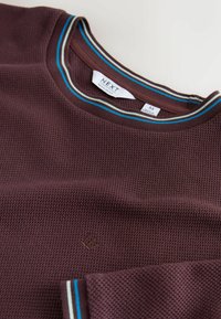 Bordo trumpomis rankovėmis marškinėliai su tekstūruota medžiaga, suapvalintu kaklu, puoštas mėlynomis ir baltomis juostelėmis bei mažuoju logotipu.