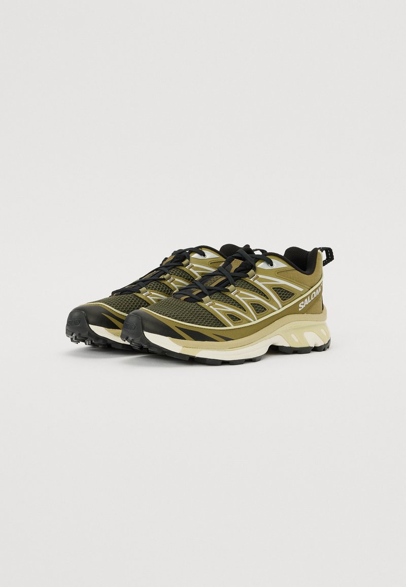 Trail-Laufschuhe mit einem Obermaterial aus schwarzem und olivgrünem Mesh, Gummisohle, strukturiertem Grip und kontrastierenden weißen Akzenten.