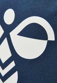 Marinblått tyg med djärva, vita grafiska mönster inklusive en cirkel och böjda former med struktur. Slätt, stickat material.