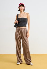 Black cropped strapless top, brown relaxed-fit pants with side stripes, grey cap, and white slip-on shoes with floral detail.