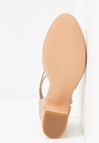 Beige Damen-Schuhsohle mit der Größe 37, glatte Vorderpartie, strukturierter Absatz und dünnen Riemen vor einem weißen Hintergrund.