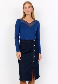 Långärmad blå topp med spetskrage, kombinerad med en mörk denimkjol med framknappar och en mittslits.