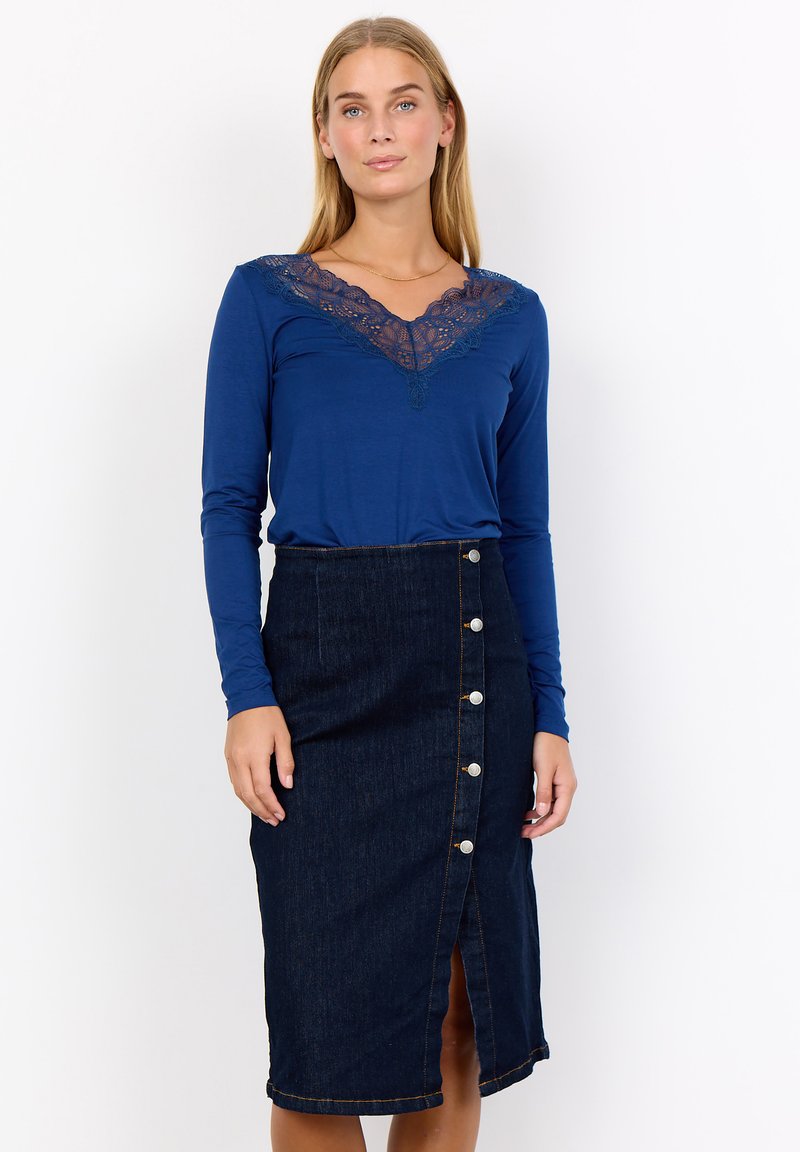 Långärmad blå topp med spetskrage, kombinerad med en mörk denimkjol med framknappar och en mittslits.