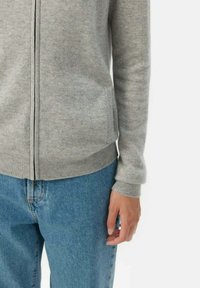 Gr�å zip-up tröja i mjukt tyg, med långa ärmar och ribbad nederkant, tillsammans med ljusblå jeans.