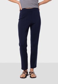 Navyblå figursydda byxor med en slät yta och ett brett midjeband, kombinerat med svarta sandaler med korsade remmar och en guldfinish.