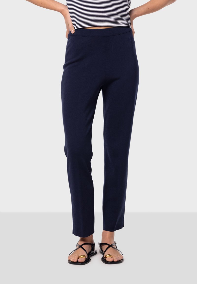 Navyblå figursydda byxor med en slät yta och ett brett midjeband, kombinerat med svarta sandaler med korsade remmar och en guldfinish.