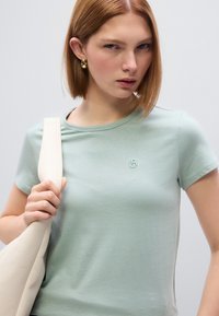 Ανοιχτοπράσινο βαμβακερό T-shirt με κοντά μανίκια και στρογγυλή λαιμόκοψη, με μικρό κεντημένο λογότυπο στο στήθος και λεία υφή.