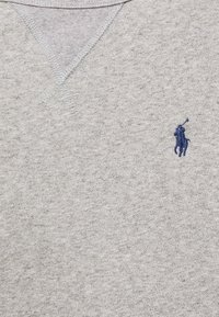 Szary bawełnowy sweter z dekoltem w serek, z małym niebieskim haftowanym logo po lewej stronie oraz teksturowanym wzorem na tkaninie.