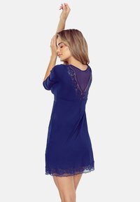Granatowa sukienka ma koronkowe plecy i dół, trzyczwarte rękawy oraz luźny krój. Tkanina ma gładką fakturę z delikatnym połyskiem.