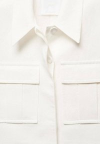 Valkoinen nappipaita, joka on valmistettu kevyestä kankaasta. Siinä on terävä kaulus, kaksi rintataskua ja hienovarainen tekstuuri. Yksinkertainen kuosi ilman kuvioita.