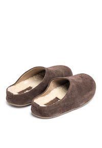 Een paar donkerbruine suède pantoffels met een crèmekleurige fluffy voering, instapmodel en platte rubberen zolen op een witte achtergrond.