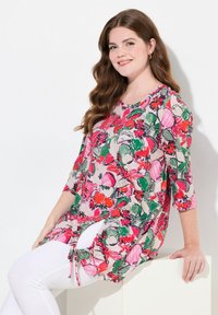 Floral tunika ylhäällä kevyestä kankaasta, jossa on kirkkaat vaaleanpunaiset, vihreät ja punaiset kuviot. Varustettu ¾-pituisilla hihoilla ja sivusiteillä helman kohdalla.