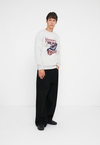 Hvit sweatshirt med en retro grafikk av "Hogwart's Express" i rødt og blått. Løs passform svarte bukser og svarte sko fullfører utseendet.