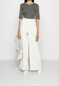 Top con estampado en blanco y negro, pantalones anchos blancos de tiro alto, zapatillas blancas y un bolso ligero con correa. Fondo de superficie plana.
