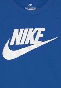 T-shirt in cotone blu con un grande logo bianco "NIKE" e design a swoosh sul davanti. Collo rotondo con una texture liscia.