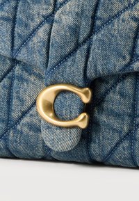 Τζιν ύφασμα σε μπλε χρώμα με λοξή ραφή σε σχέδιο καπιτονέ και χρυσό μεταλλικό κούμπωμα σε σχήμα γράμματος C σε τ σάντα.