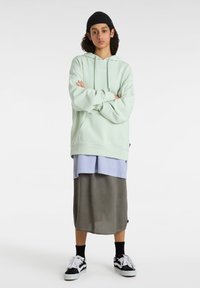 Mint green hoodie with a kangaroo pocket, layered over a light blue shirt and gray skirt. Complements black sneakers and beanie.