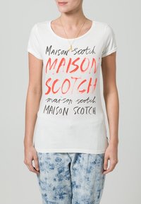 Hvid bomulds t-shirt med grafisk tryk med teksten "Maison Scotch" i forskellige farver. Korte ærmer med rund halsudskæring.