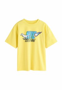 Gul bomulds T-shirt med korte ærmer. Har et grafisk design med "NYC" og "SKATE OF MIND," der viser en dinosaur på et skateboard.