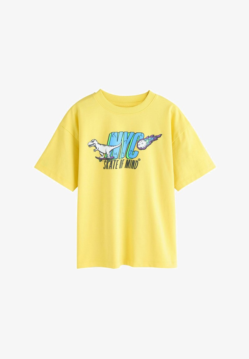 Žluté bavlněné tričko s grafikou dinosaura na skateboardu a textem "NYC SKATE OF MIND" v modré a černé barvě. Krátké rukávy.