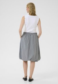 Top blanco sin mangas con bordes con volantes, combinado con una falda de rayas de longitud a la rodilla en gris y blanco, que cuenta con una cinturilla elástica.