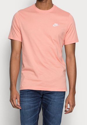 Kurzärmeliges T-Shirt mit Rundhalsausschnitt aus hellrosa Baumwolle mit weißem Nike-Logo auf der Brust. Kombiniert mit blauen Jeans aus Denim.